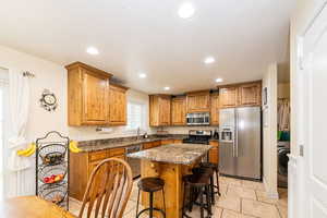 Kitchen featuring appliances with stainless steel finishes, brown cabinets, a breakfast bar area, a sink, and light tile patterned floors