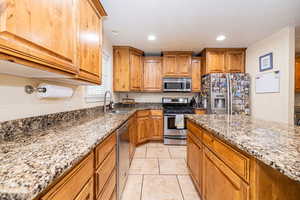 Kitchen featuring stainless steel appliances, a sink, light stone countertops, brown cabinets, and recessed lighting