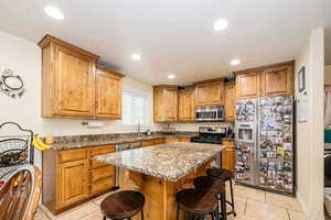 Kitchen with appliances with stainless steel finishes, a sink, light tile patterned floors, a kitchen bar, and recessed lighting
