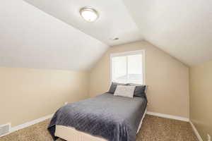 Bedroom with carpet, vaulted ceiling, baseboards, and a textured ceiling