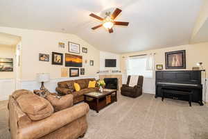 Living area featuring lofted ceiling, ceiling fan, light carpet, a wainscoted wall, and a tiled fireplace