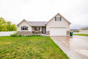View of front of house with stone siding, stucco siding, a garage, driveway, and covered porch
