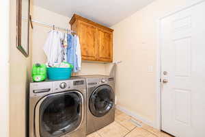 Washroom with washing machine and dryer, light tile patterned floors, cabinet space, and baseboards