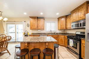 Kitchen featuring appliances with stainless steel finishes, light tile patterned flooring, a sink, a kitchen breakfast bar, and a center island