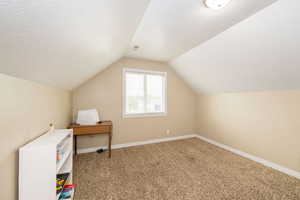 Bonus room featuring lofted ceiling, carpet flooring, baseboards, and a textured ceiling