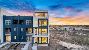 Back of house at dusk featuring a balcony and stucco siding