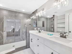 Bathroom featuring a stall shower, double vanity, tile patterned flooring, tile walls, and a chandelier