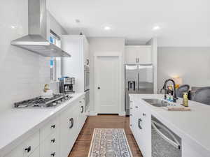 Kitchen with wall chimney exhaust hood, a sink, appliances with stainless steel finishes, tasteful backsplash, and dark wood-style floors