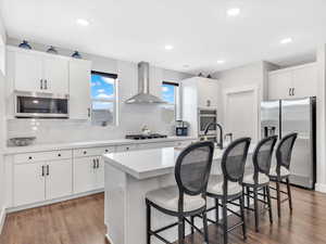 Kitchen with stainless steel appliances, wall chimney exhaust hood, a kitchen bar, decorative backsplash, and light countertops