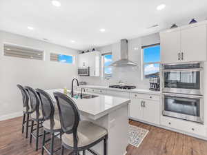 Kitchen featuring wall chimney exhaust hood, appliances with stainless steel finishes, a sink, a breakfast bar, and recessed lighting
