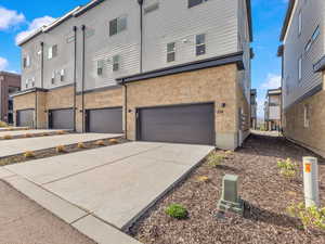 Back of house featuring an attached garage, concrete driveway, and stone siding