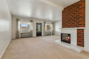 Unfurnished living room with radiator, a multi sided fireplace, carpet floors, and baseboards