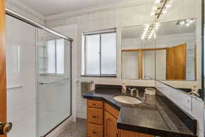 Bathroom featuring a shower stall, ornamental molding, vanity, and tile walls