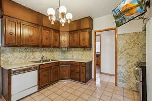 Kitchen with white dishwasher, a sink, double oven range, light countertops, and a chandelier