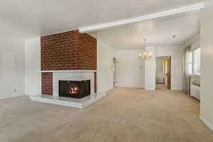Unfurnished living room with a chandelier, radiator heating unit, a fireplace, carpet floors, and beamed ceiling