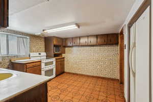 Kitchen featuring range with two ovens, stainless steel microwave, light countertops, and brown cabinetry