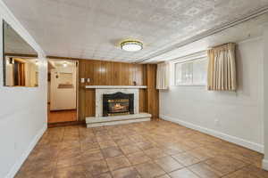 Unfurnished living room with a glass covered fireplace, baseboards, wooden walls, an ornate ceiling, and crown molding