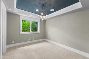 Carpeted empty room featuring a tray ceiling, a chandelier, and crown molding