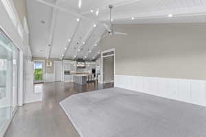 Living area featuring high vaulted ceiling, dark wood finished floors, a ceiling fan, beamed ceiling, and a wainscoted wall