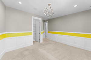 Carpeted spare room with a decorative wall, wainscoting, recessed lighting, and a chandelier
