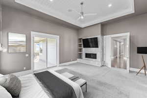 Carpeted bedroom featuring access to exterior, a raised ceiling, recessed lighting, a glass covered fireplace, and ceiling fan
