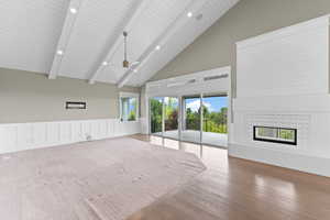 Unfurnished living room featuring high vaulted ceiling, a tiled fireplace, wood finished floors, beamed ceiling, and a ceiling fan