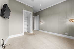 Unfurnished bedroom with carpet floors, baseboards, a spacious closet, ornamental molding, and a decorative wall