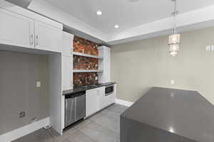 Bar area with dark countertops, open shelves, white cabinetry, pendant lighting, and stainless steel appliances