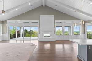 Unfurnished living room with wood finished floors, high vaulted ceiling, beamed ceiling, a decorative wall, and a glass covered fireplace