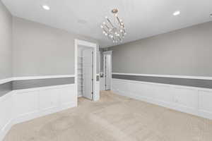 Empty room featuring light carpet, a decorative wall, wainscoting, a chandelier, and recessed lighting