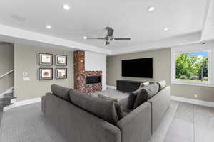 Tiled living room featuring a brick fireplace, stairway, ceiling fan, recessed lighting, and a tray ceiling