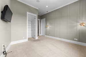 Unfurnished bedroom featuring light colored carpet, crown molding, and a walk in closet