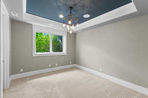 Carpeted empty room featuring a raised ceiling, a chandelier, and baseboards