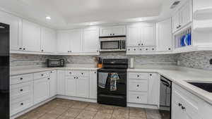 Kitchen with black appliances, white cabinetry, light tile patterned floors, backsplash, and light countertops