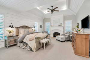 Bedroom featuring carpet floors, lofted ceiling, a fireplace, wood walls, and a ceiling fan
