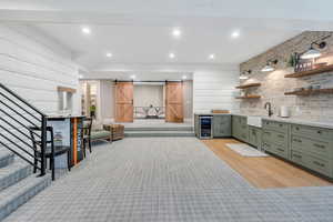 Bar area with wine cooler, a barn door, a sink, stairs, and light wood-type flooring