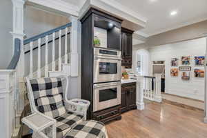 Kitchen with stainless steel double oven, light wood finished floors, dark brown cabinets, crown molding, and recessed lighting