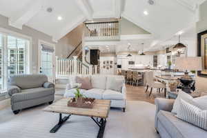 Living room featuring beamed ceiling, stairway, wood finished floors, high vaulted ceiling, and a chandelier