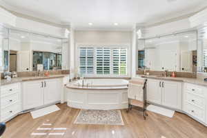Bathroom with ornamental molding, wood finished floors, a bath, and two vanities
