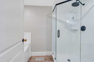 Bathroom with a stall shower, wood finished floors, a garden tub, and baseboards
