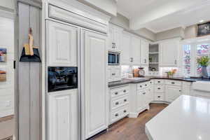 Kitchen with stainless steel microwave, paneled fridge, open shelves, white cabinetry, and crown molding