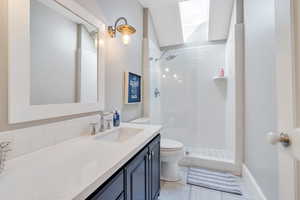 Full bath featuring toilet, tiled shower, vanity, and a skylight