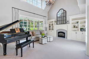Living room featuring a towering ceiling, carpet, a chandelier, healthy amount of natural light, and a fireplace with raised hearth