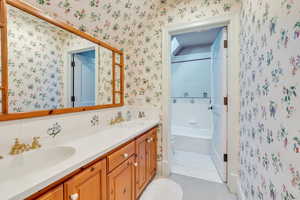 Bathroom with wallpapered walls, tile patterned floors, double vanity, and toilet