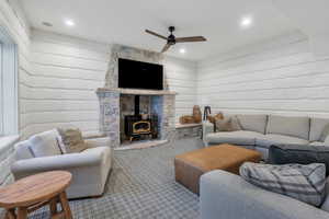 Carpeted living room with a wood stove, a ceiling fan, wooden walls, and recessed lighting