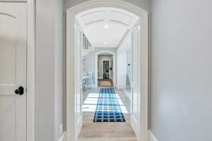 Hall with arched walkways, light wood-style floors, and recessed lighting