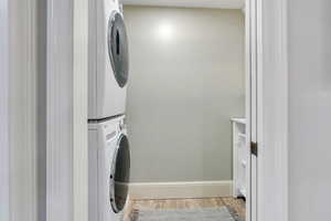 Laundry area featuring stacked washing machine and dryer, light wood finished floors, and baseboards