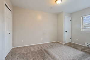 Unfurnished bedroom with carpet flooring, baseboards, and a baseboard heating unit