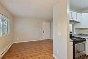 Kitchen with stainless steel electric range, a baseboard heating unit, light wood-type flooring, under cabinet range hood, and light countertops