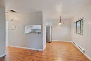 Unfurnished living room with baseboard heating, light wood-style floors, and baseboards